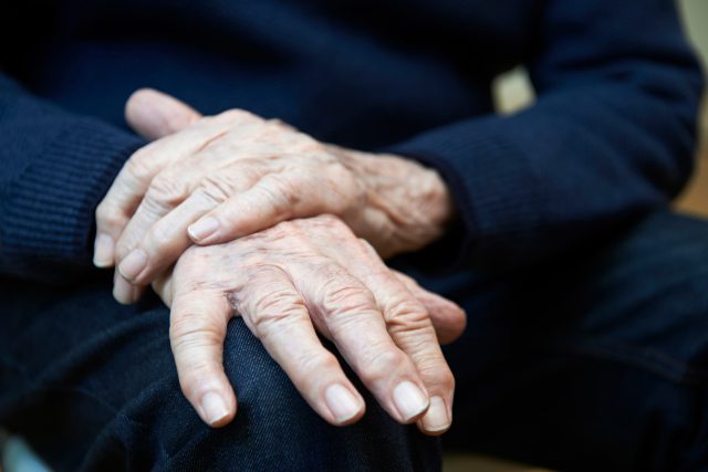 Zdjęcie rąk starszej osoby, cierpiącej na chorobę Parkinsona.