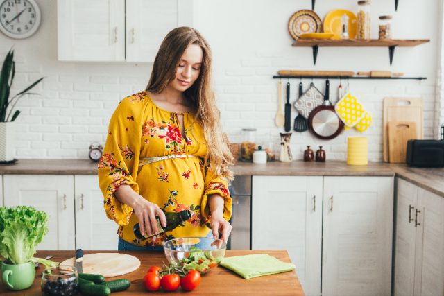 Kobieta w ciąży robiąca posiłek w kuchni.