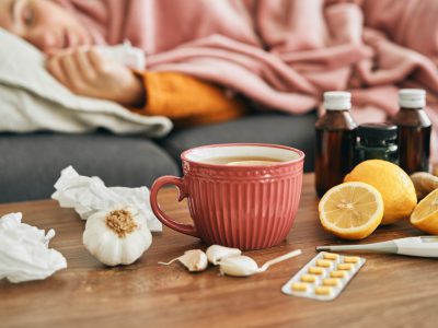Chora leząca osoba z kubkiem herbaty, czosnkiem, cytryną i lekami na stoliku