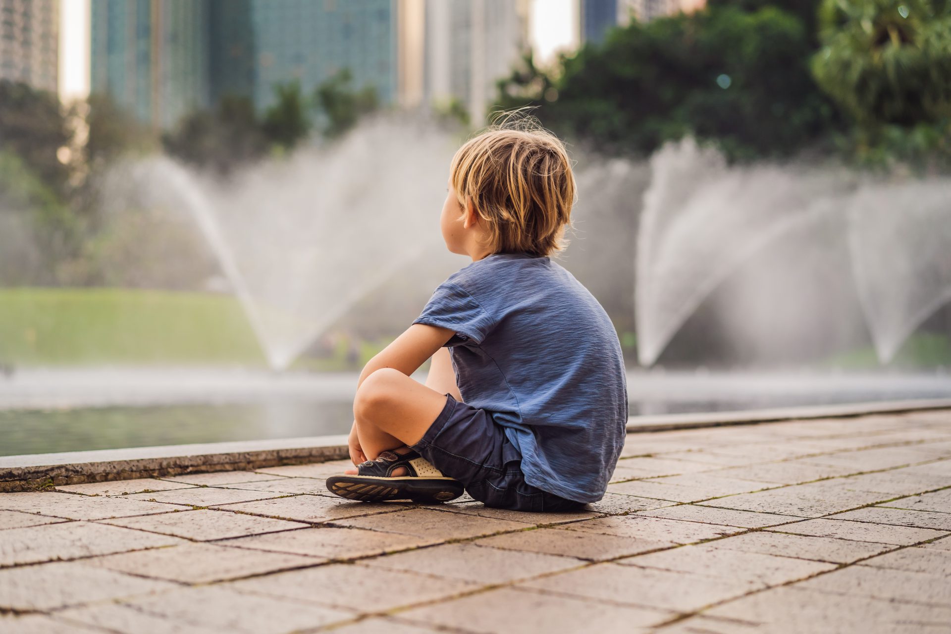 Samotnie siedzące dziecko przy miejskiej fontannie.
