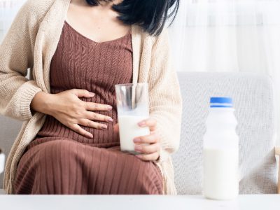 Kobieta trzymająca się za brzuch jedną ręką, a w drugiej trzymająca szklankę z mlekiem