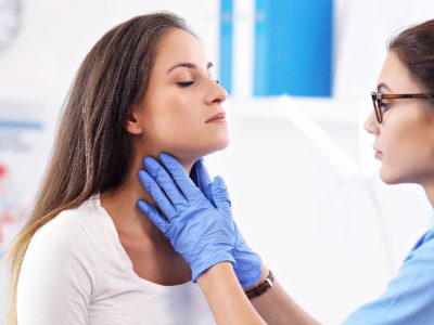 Lekarka trzymająca kobietę za szyję w celu badania przerostu migdałka gardłowego